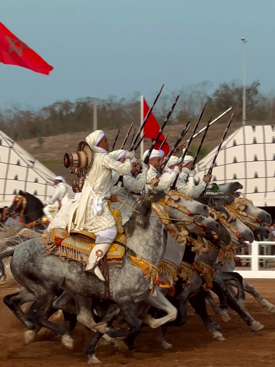 Moroccan horsemen in white djellabas and red fez hats with decorated horses and flags