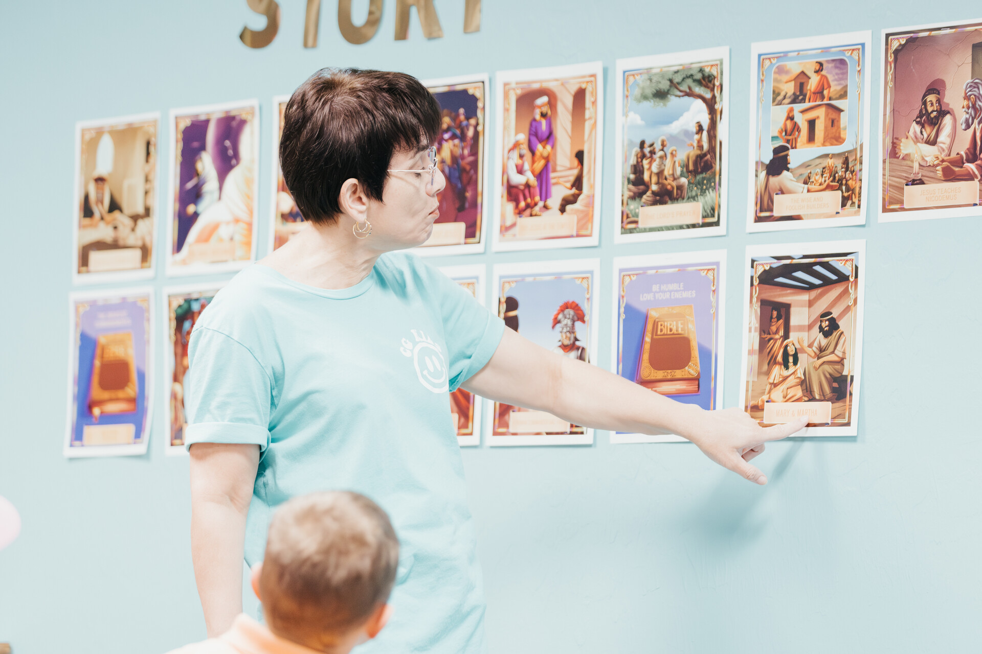 CG Kids teacher pointing to Bible story cards on the wall