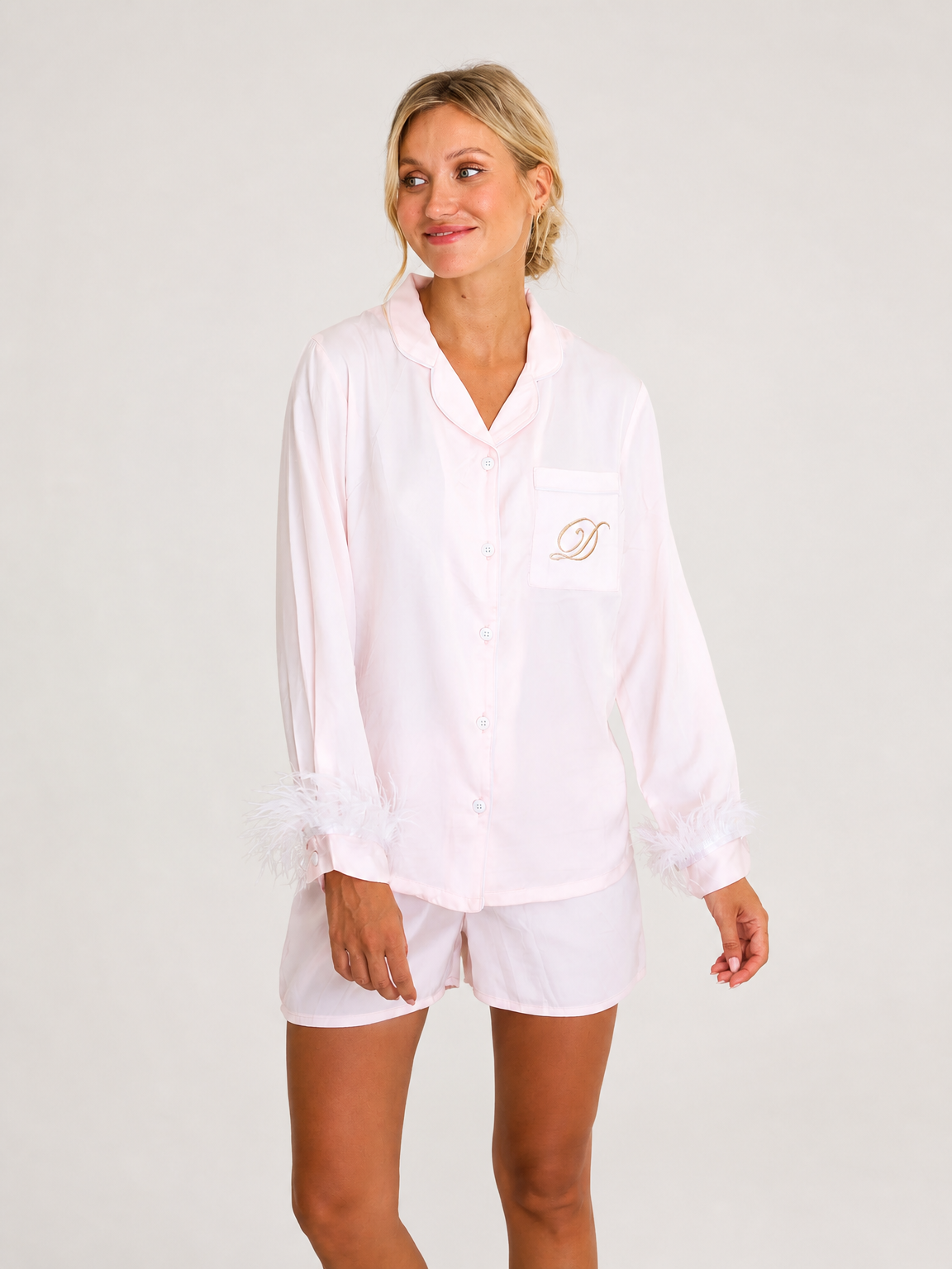 A satin blush button-front sleep shirt and shorts with feather-trimmed cuffs and a monogram detail on the chest pocket.