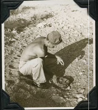 A man crouches beside the detector, clearing soil from rocky ground.