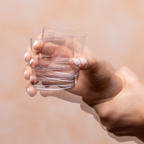 A close-up of a hand holding a glass of water while using the other hand to steady it against tremors
