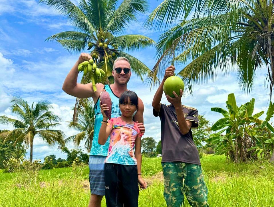 Mężczyzna z dziećmi trzymające kokosy na tropikalnym polu