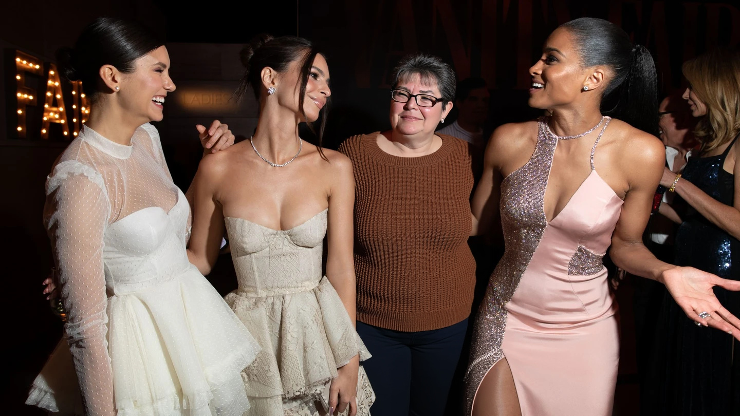 Middle-aged woman in brown sweater with three glamorous celebrities at an event