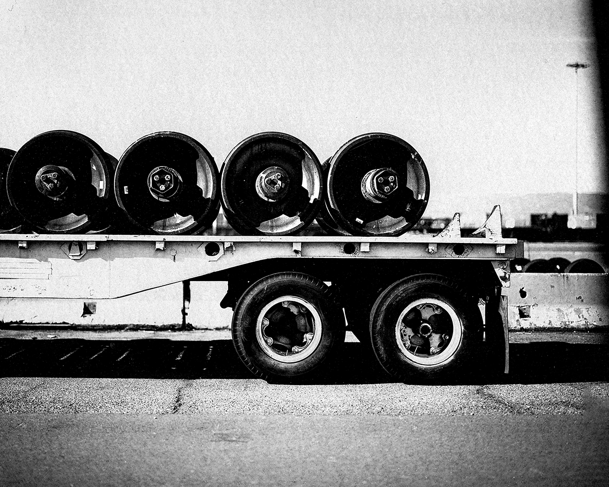 Flatbed truck loaded with four large industrial wheels or turbine components in geometric horizontal arrangement with clear sky