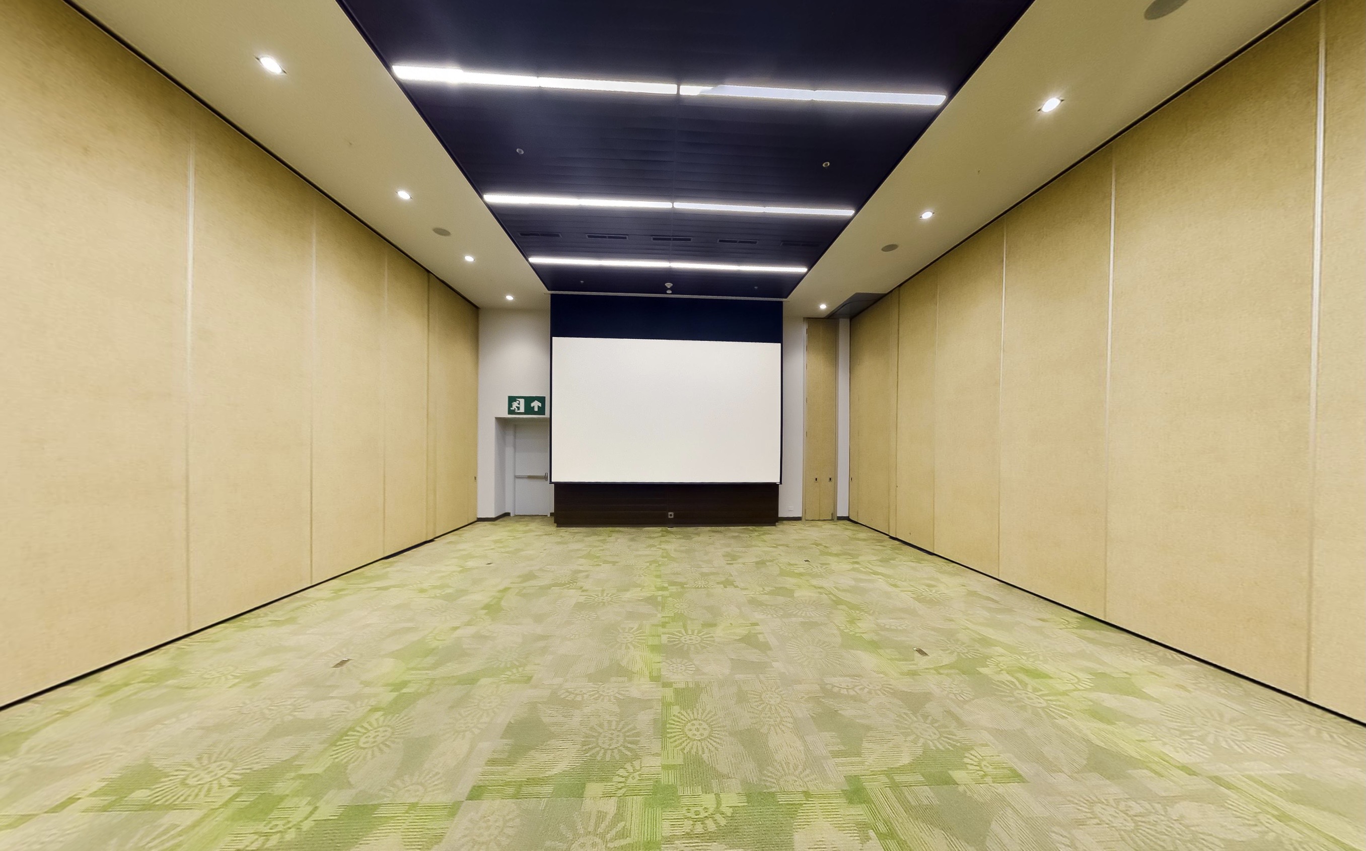 Convention center room with operable partition walls lining both sides, projection screen, and green patterned carpet