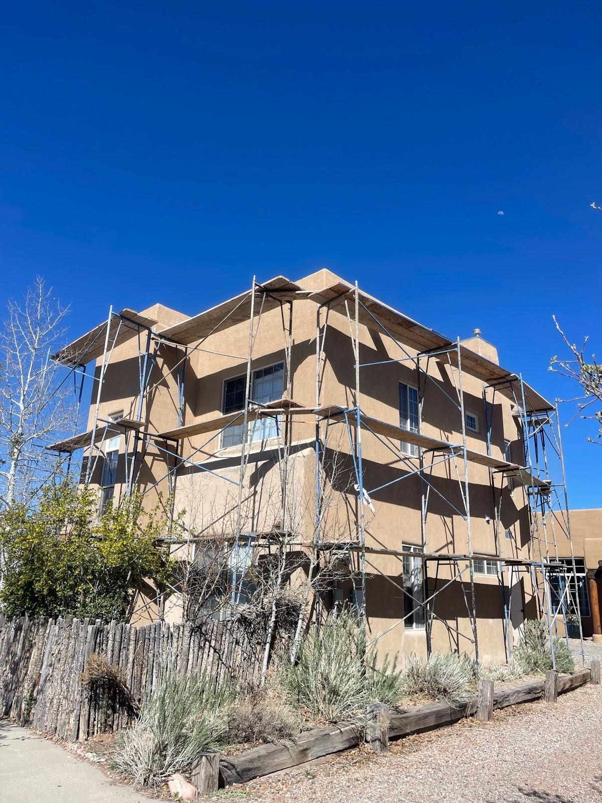 Multi-story stucco home with scaffolding during exterior refinishing
