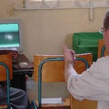 Ordensschwester erklärt etwas vor einem laufenden CRT-Monitor im Klassenraum