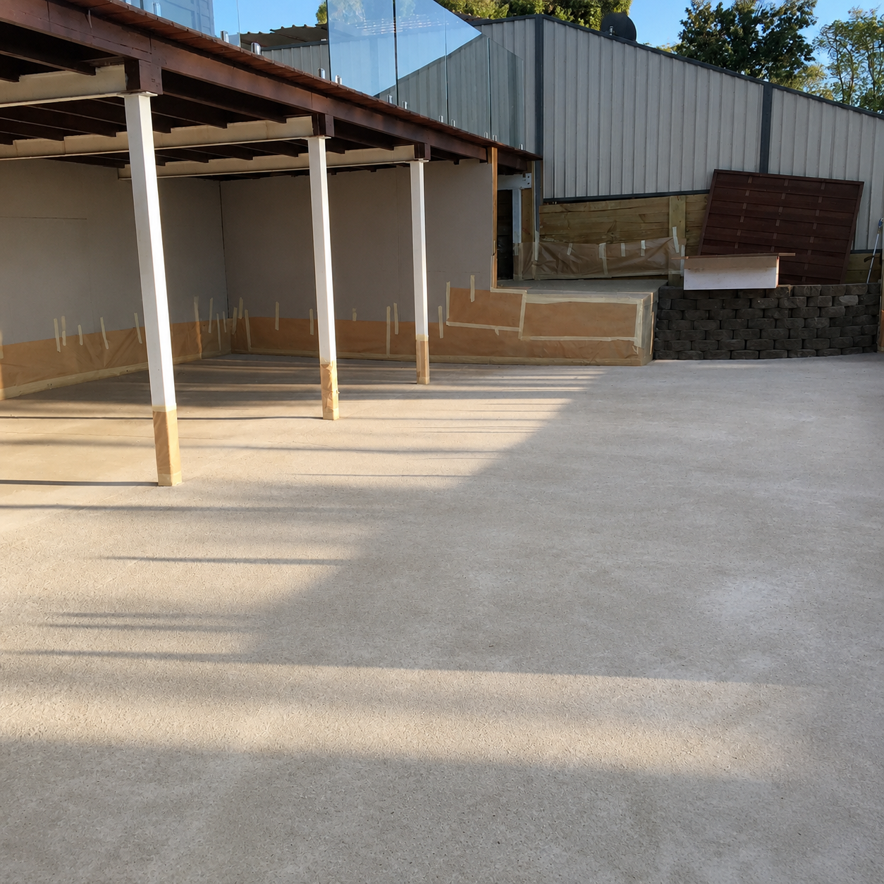 Plain untreated concrete patio under a carport, masked up and prepared before Spray Crete resurfacing