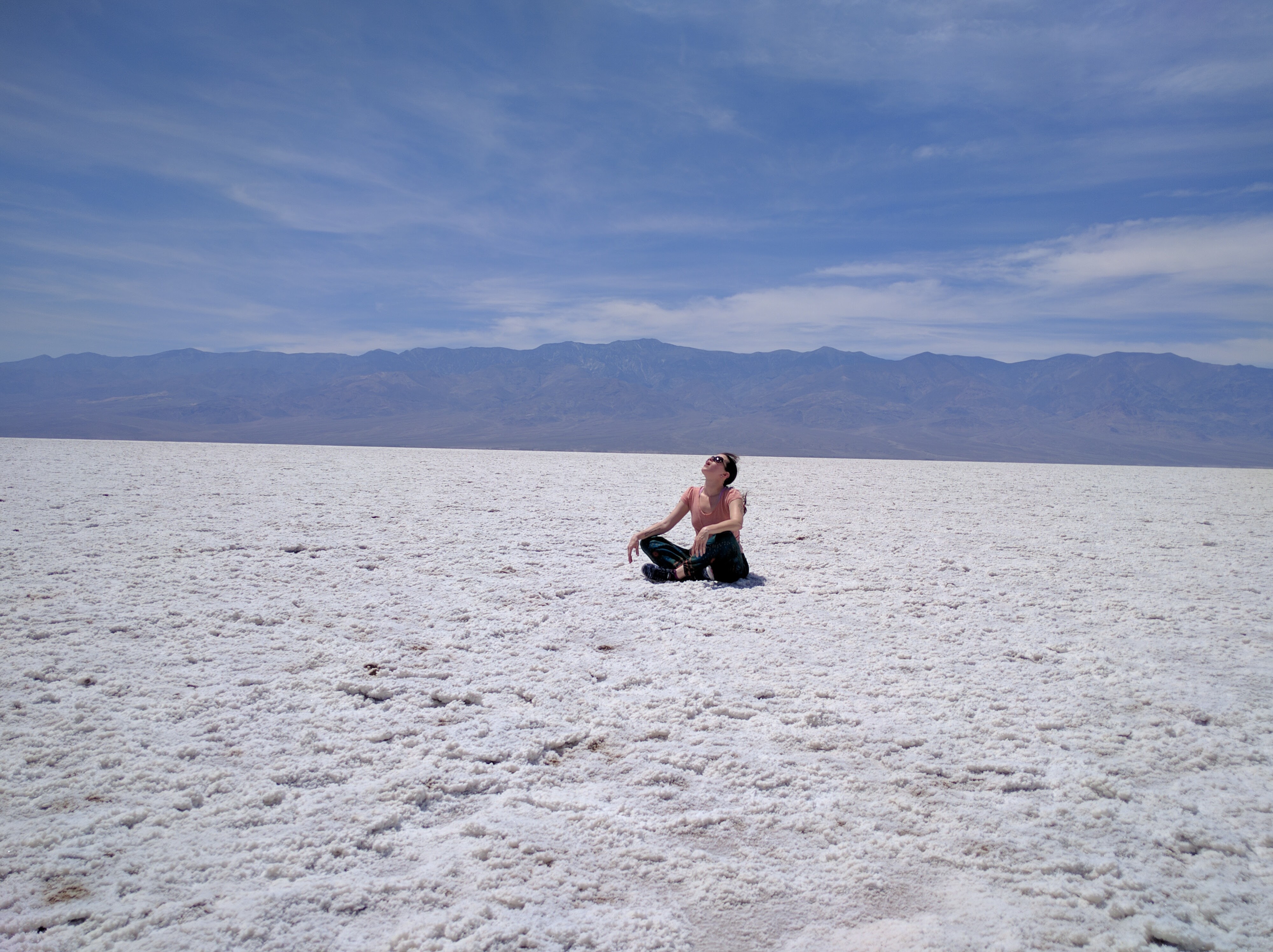 Person sitting on salt flats with mountains in background