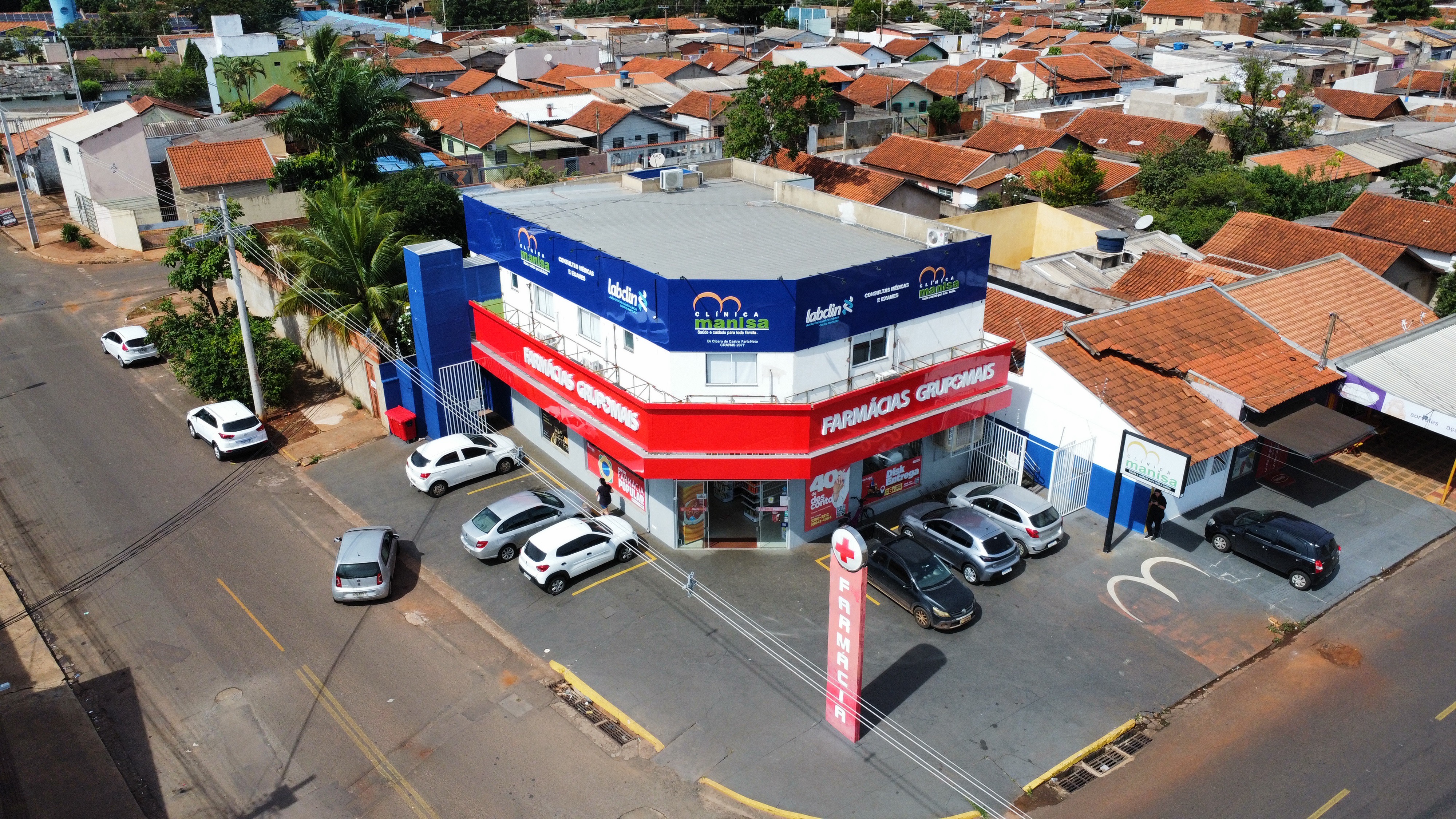 Vista aérea da Clínica Manisa - Prédio de esquina com fachada azul e vermelha, ao lado da Farmácias Grupomais