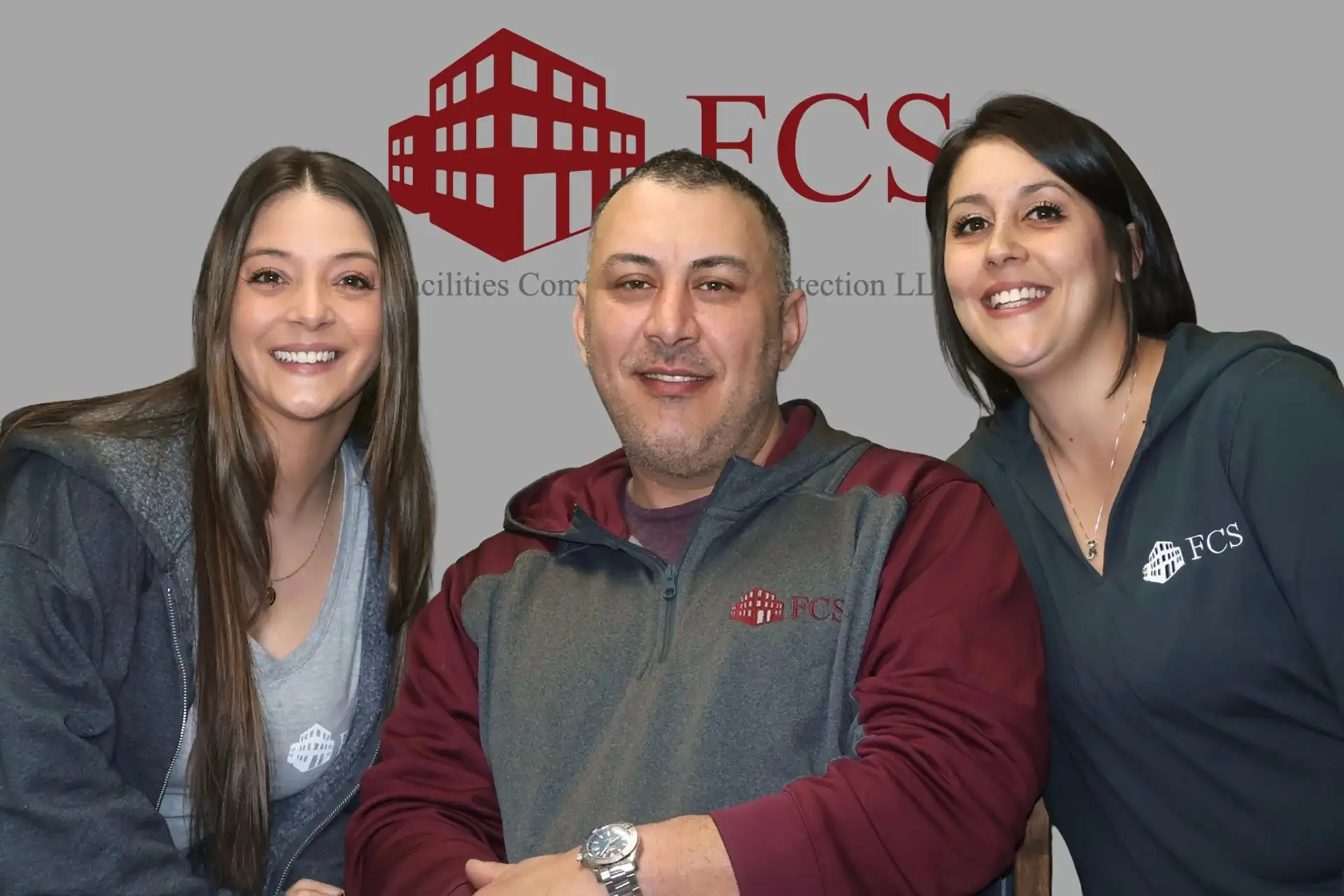 FCS team members smiling in front of FCS logo backdrop