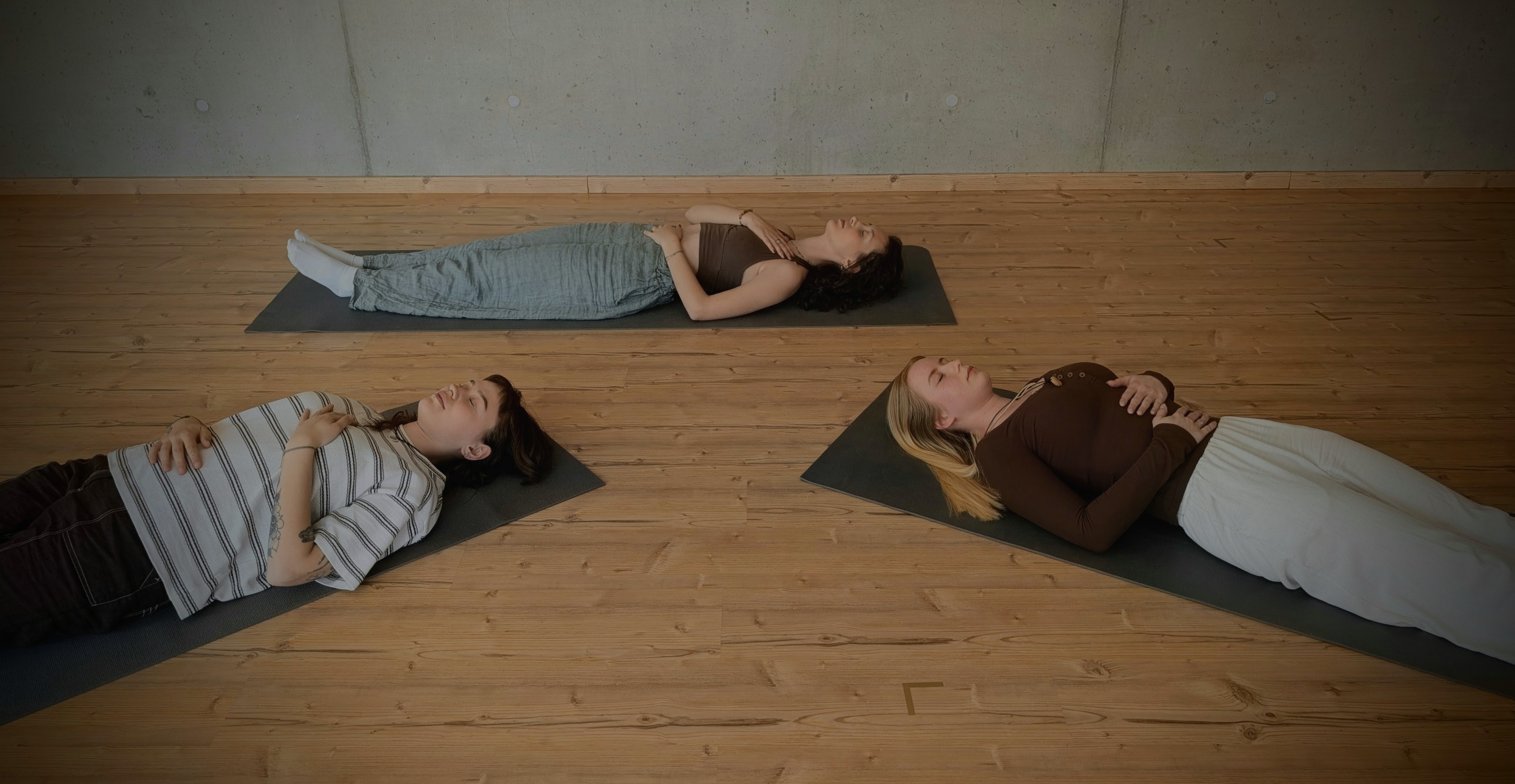 Three women lying on yoga mats in triangle formation