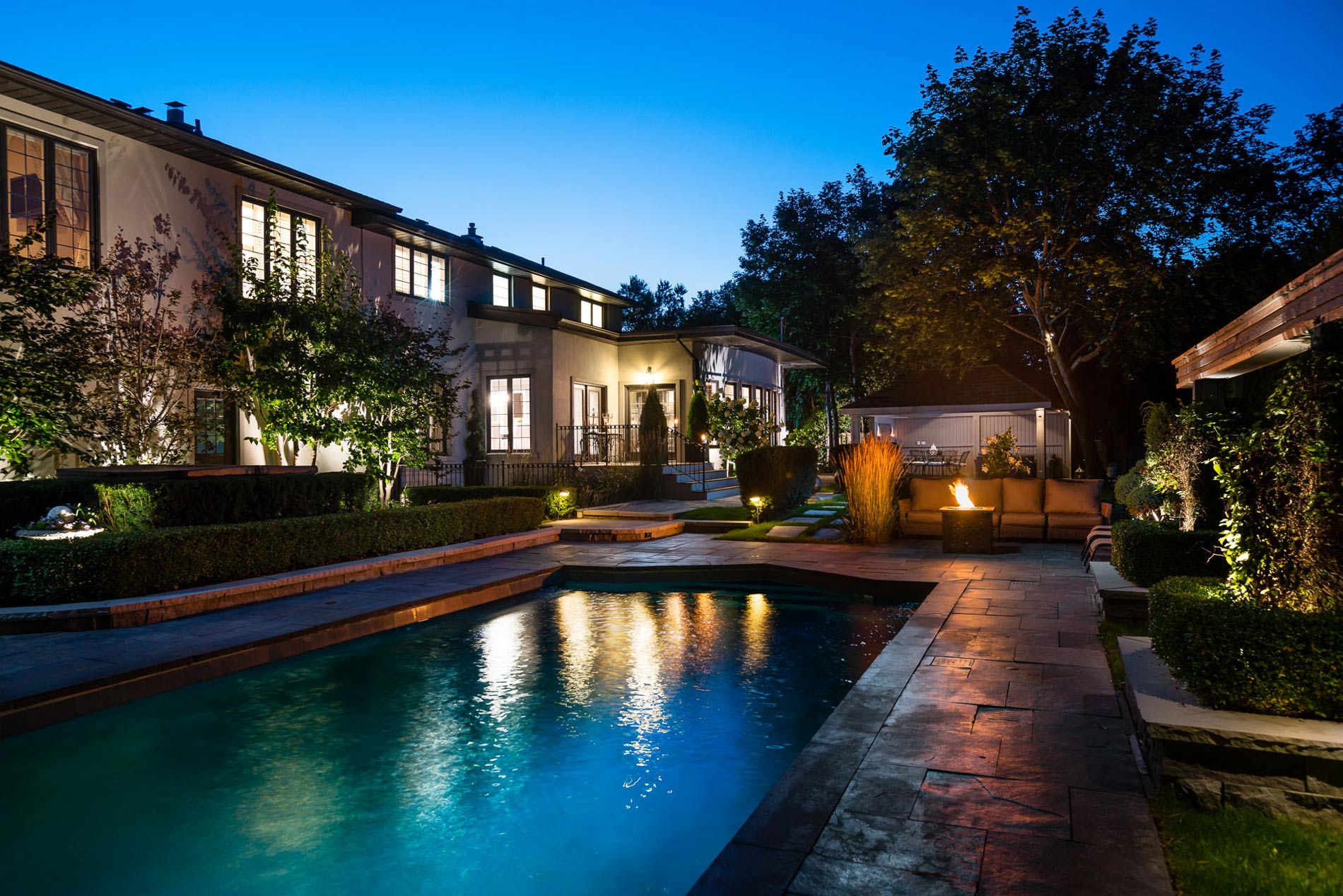 Luxury home exterior at dusk with a lit pool and landscaped patio