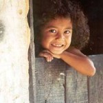 Kind schaut lächelnd um einen Türpfosten