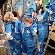Gruppe in blauen Overalls vor bemaltem Container