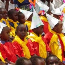 Kinder in roten und gelben Umhängen mit Papierhüten beim Schulfest