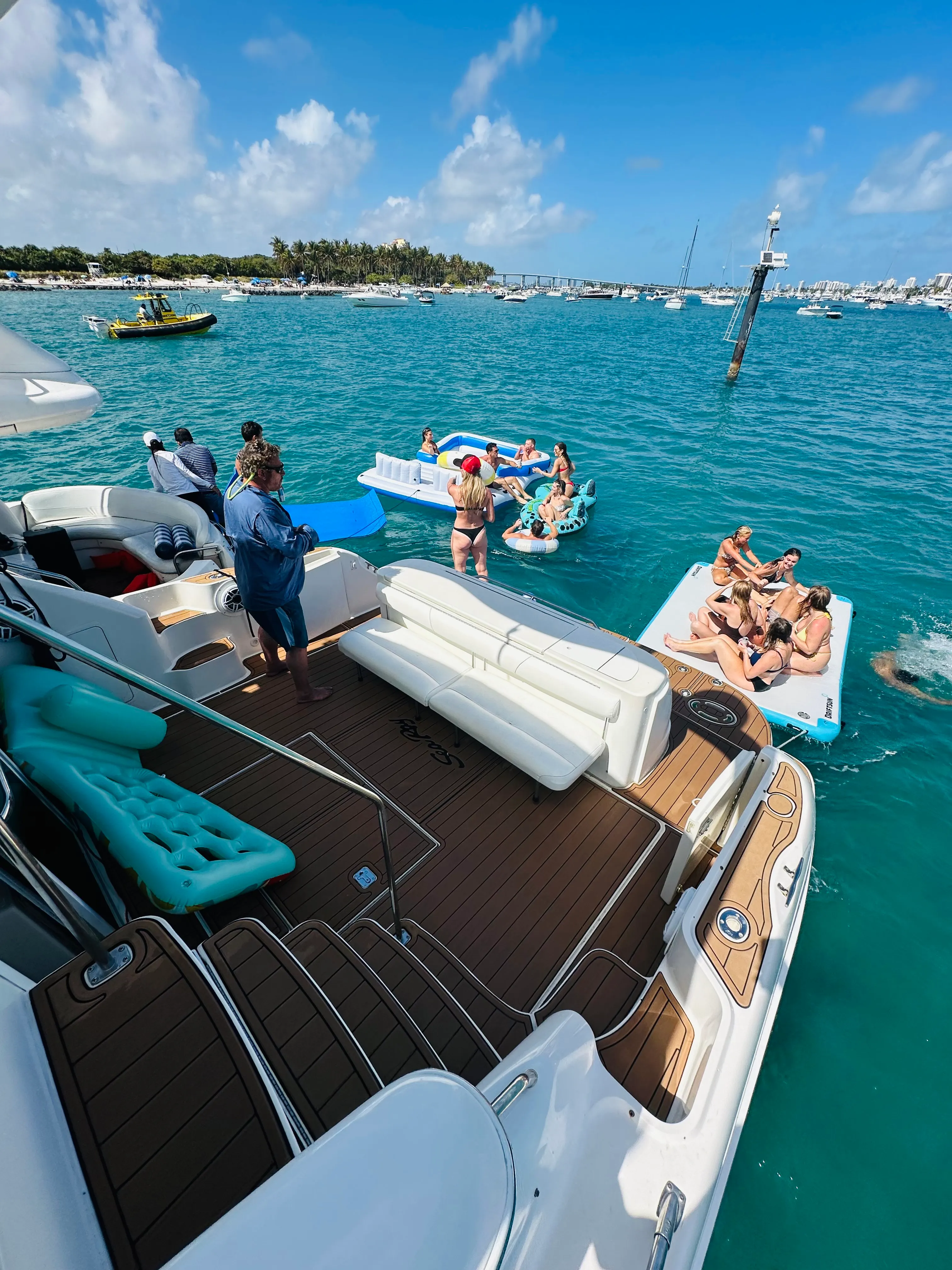 Guests relaxing on floats and a swim platform anchored at the sandbar in turquoise water