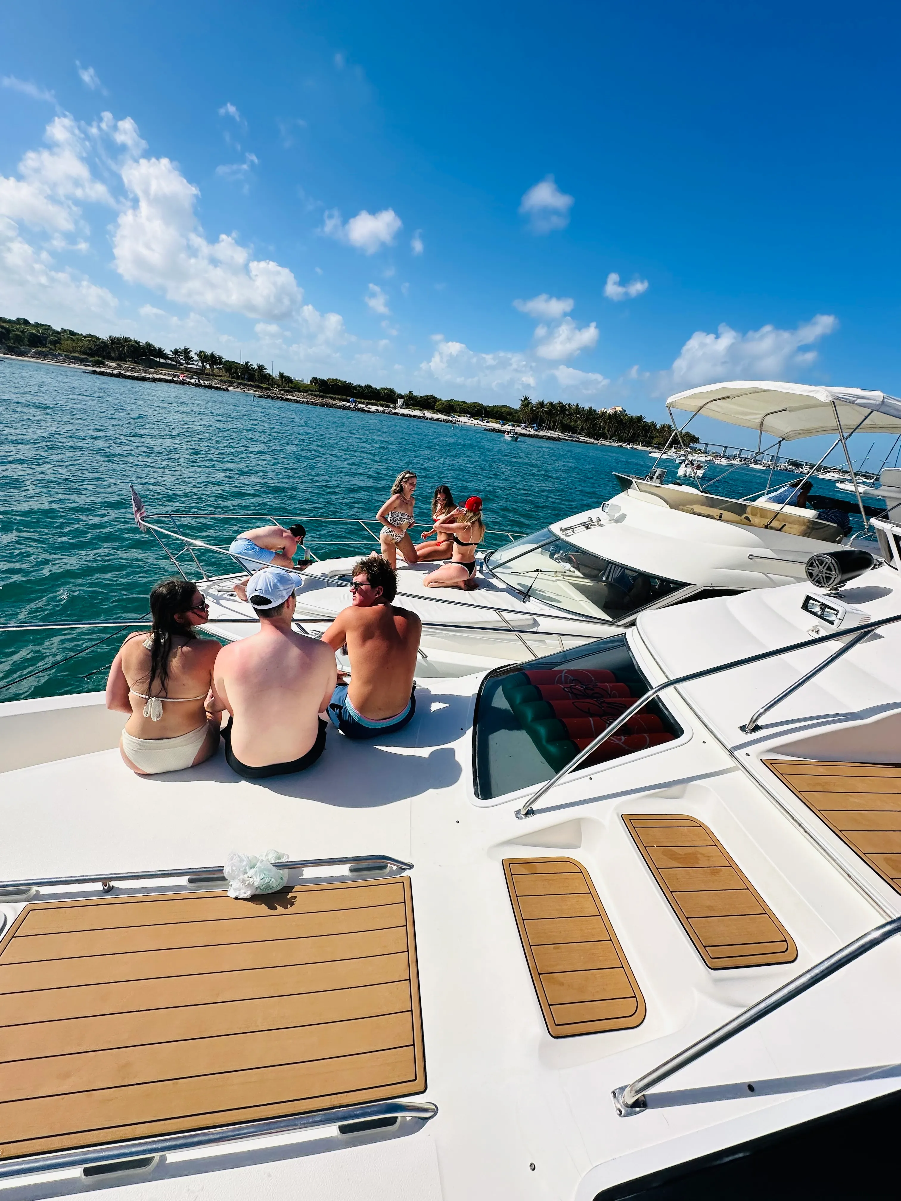 Friend group lounging on the yacht cabin rooftop at anchor in turquoise water