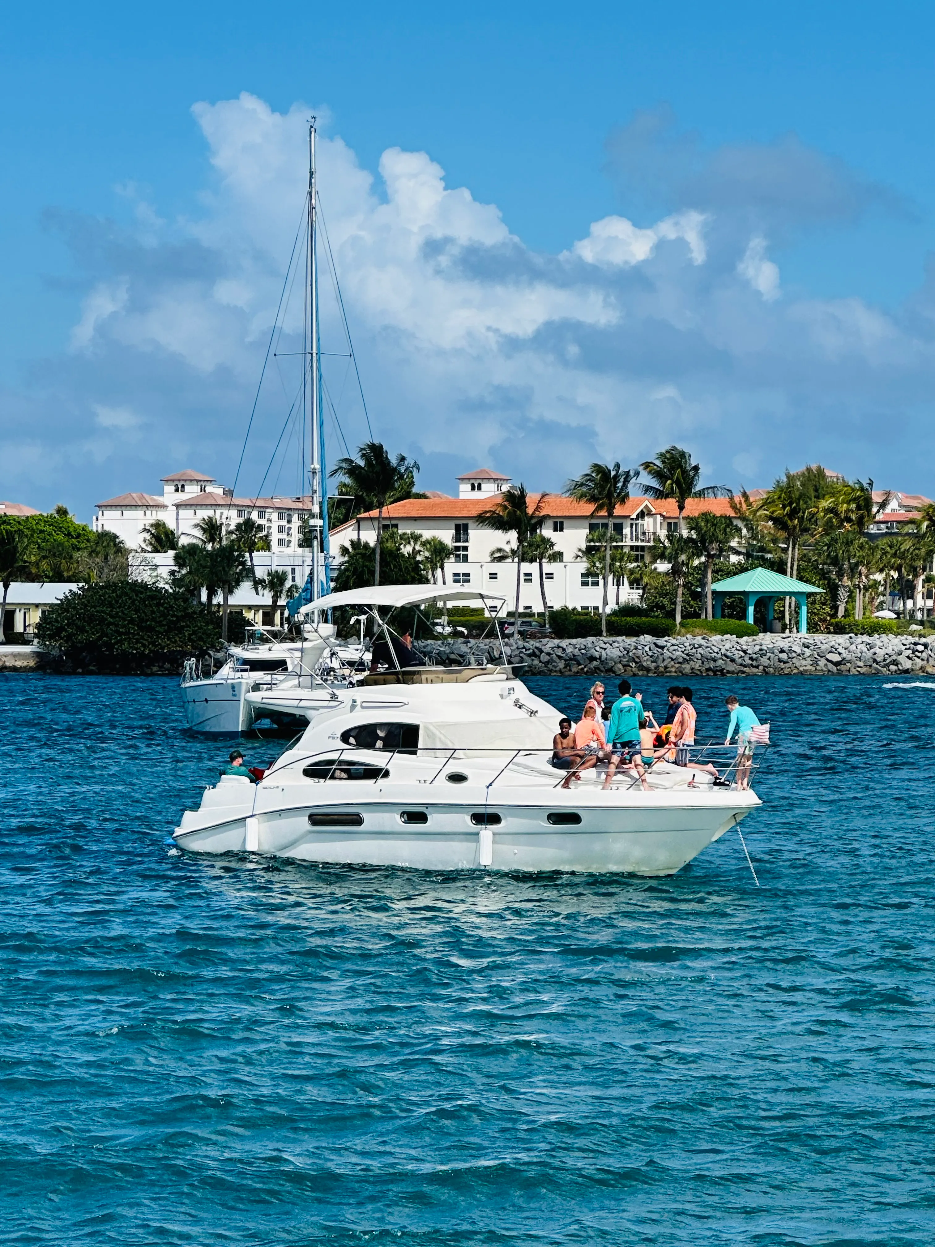 Yacht anchored near a Palm Beach luxury estate with group of guests on the stern in turquoise water