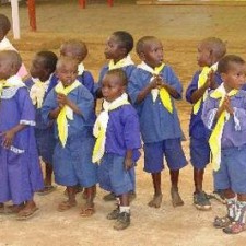 Kleine Kinder in blauen Schuluniformen mit gelben Halstüchern stehen in einer Reihe