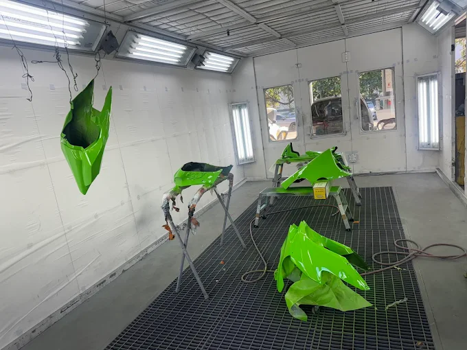 Custom lime-green Kawasaki motorcycle fairings hanging in the Factory Finish paint booth