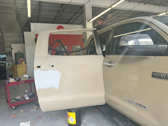 Tan Toyota Tundra mid-repair with primer applied to the door inside the Factory Finish shop