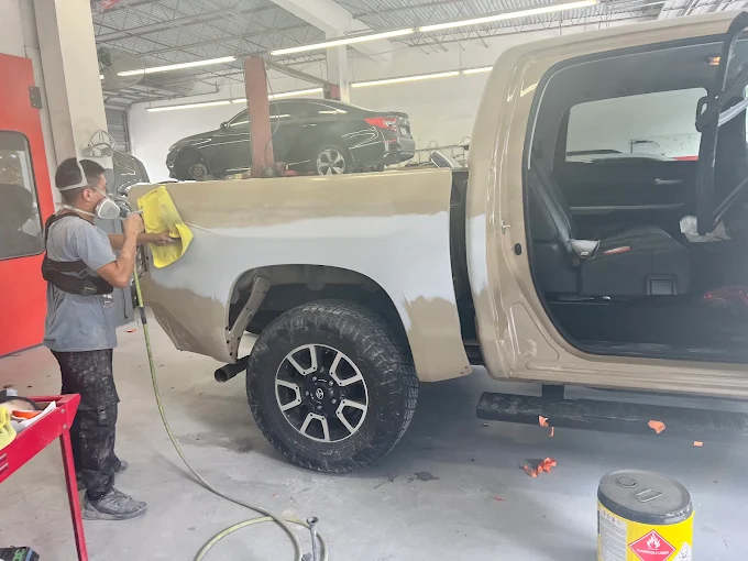 Factory Finish technician in protective gear spraying paint on a Toyota Tundra rear panel inside the booth