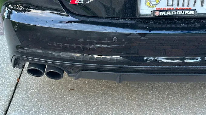 Close-up of a black Audi rear bumper with dual exhaust tips and surface scuffing at Factory Finish