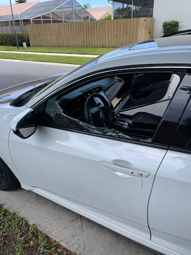 White Honda Civic with a shattered driver-side window awaiting collision repair at Factory Finish