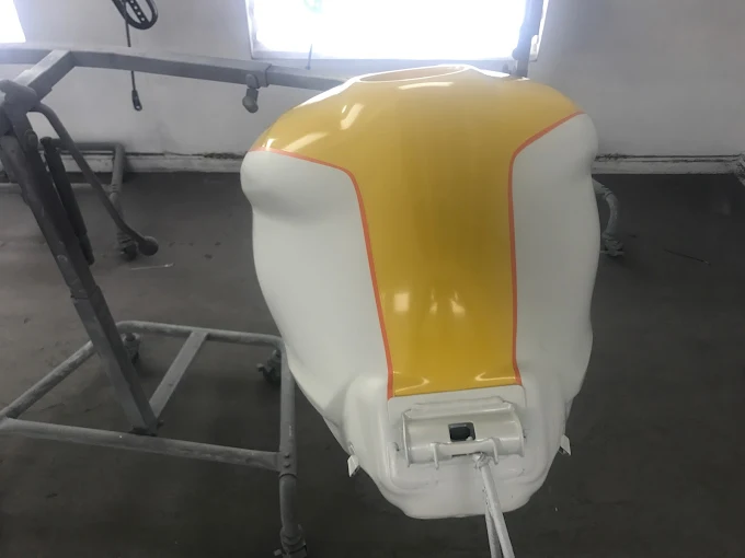 Custom-painted motorcycle fuel tank with white and yellow finish hanging in the Factory Finish paint booth