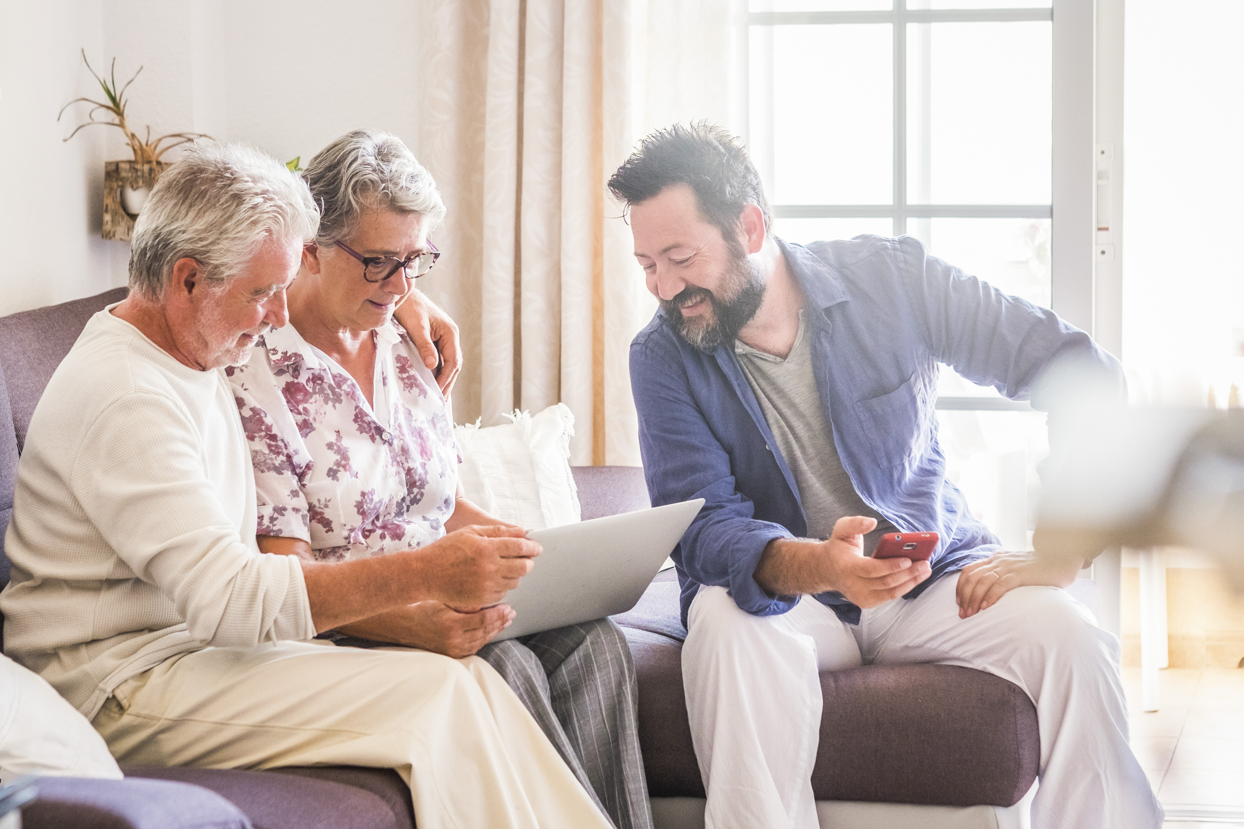 Adult child sitting with aging parents at home, looking at a laptop together