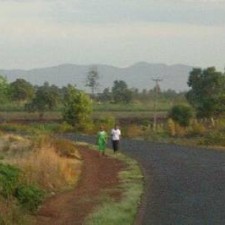 Zwei Personen spazieren auf einer asphaltierten Straße mit Hügeln im Hintergrund