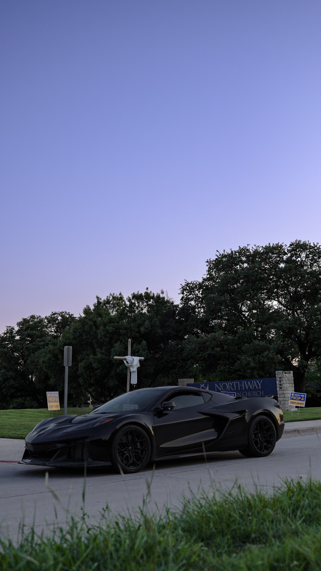 Black C8 Corvette at dusk with purple twilight sky and trees in background
