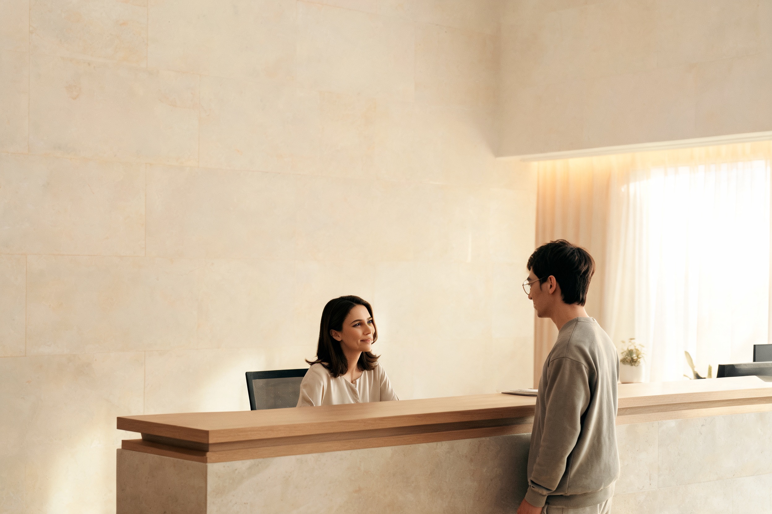 A calm clinic reception desk in soft, natural light with two people talking