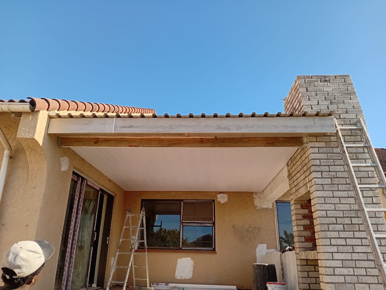 After: Flat roof installation Gqeberha — completed white PVC ceiling fitted under timber beams, clean soffit with fascia, brick column and blue sky
