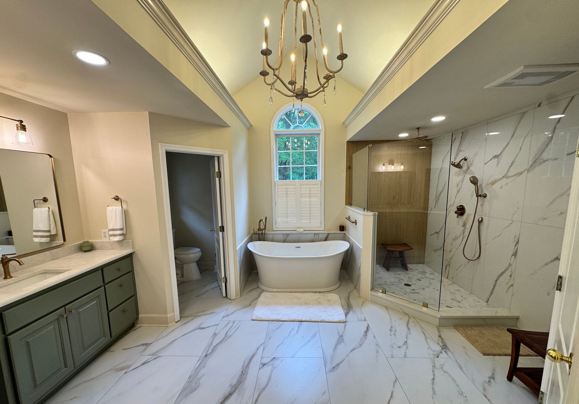 Luxurious remodeled bathroom with a freestanding soaking tub, marble flooring, glass walk-in shower, and a chandelier