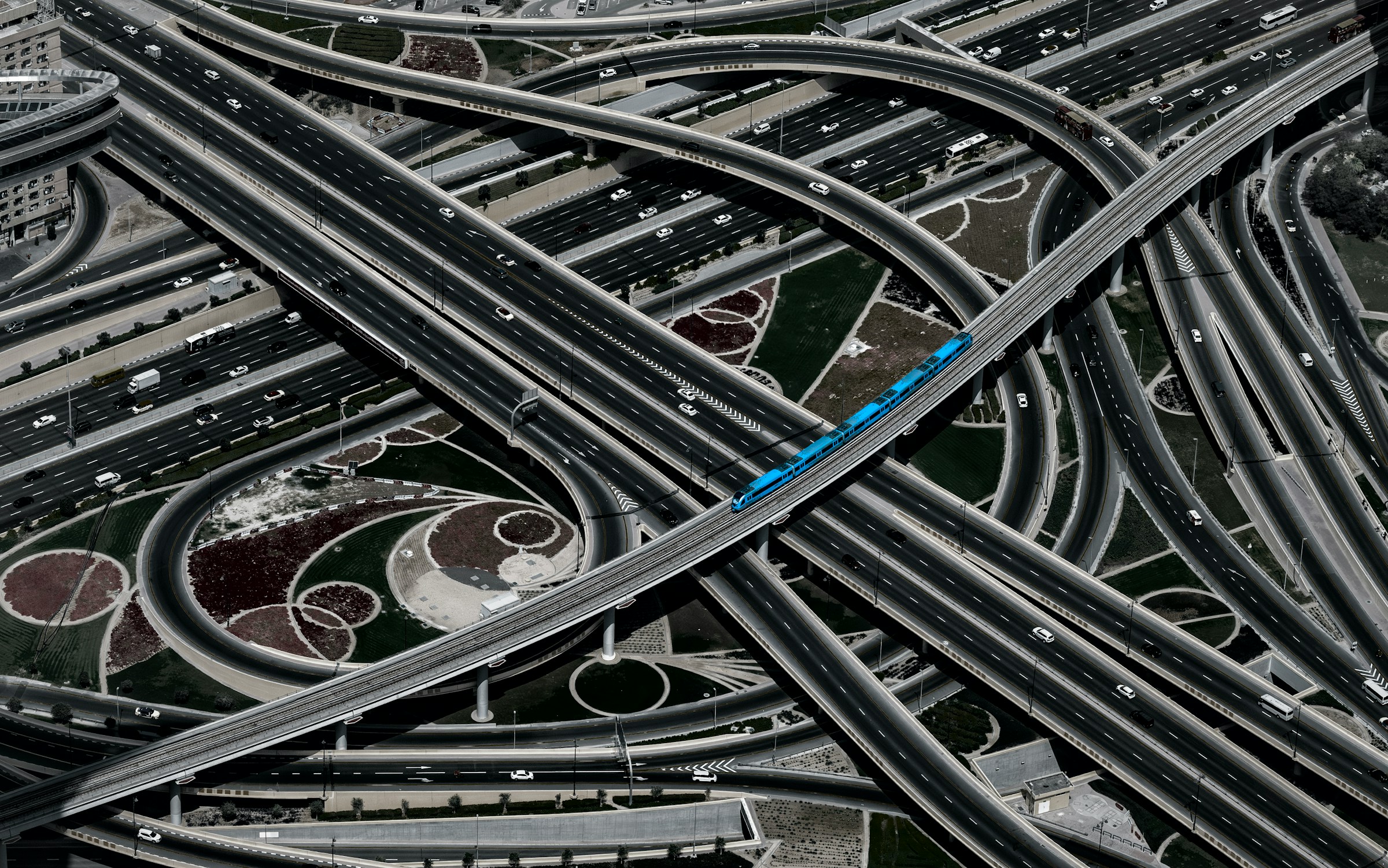 Aerial view of complex highway interchange in Dubai with blue metro train