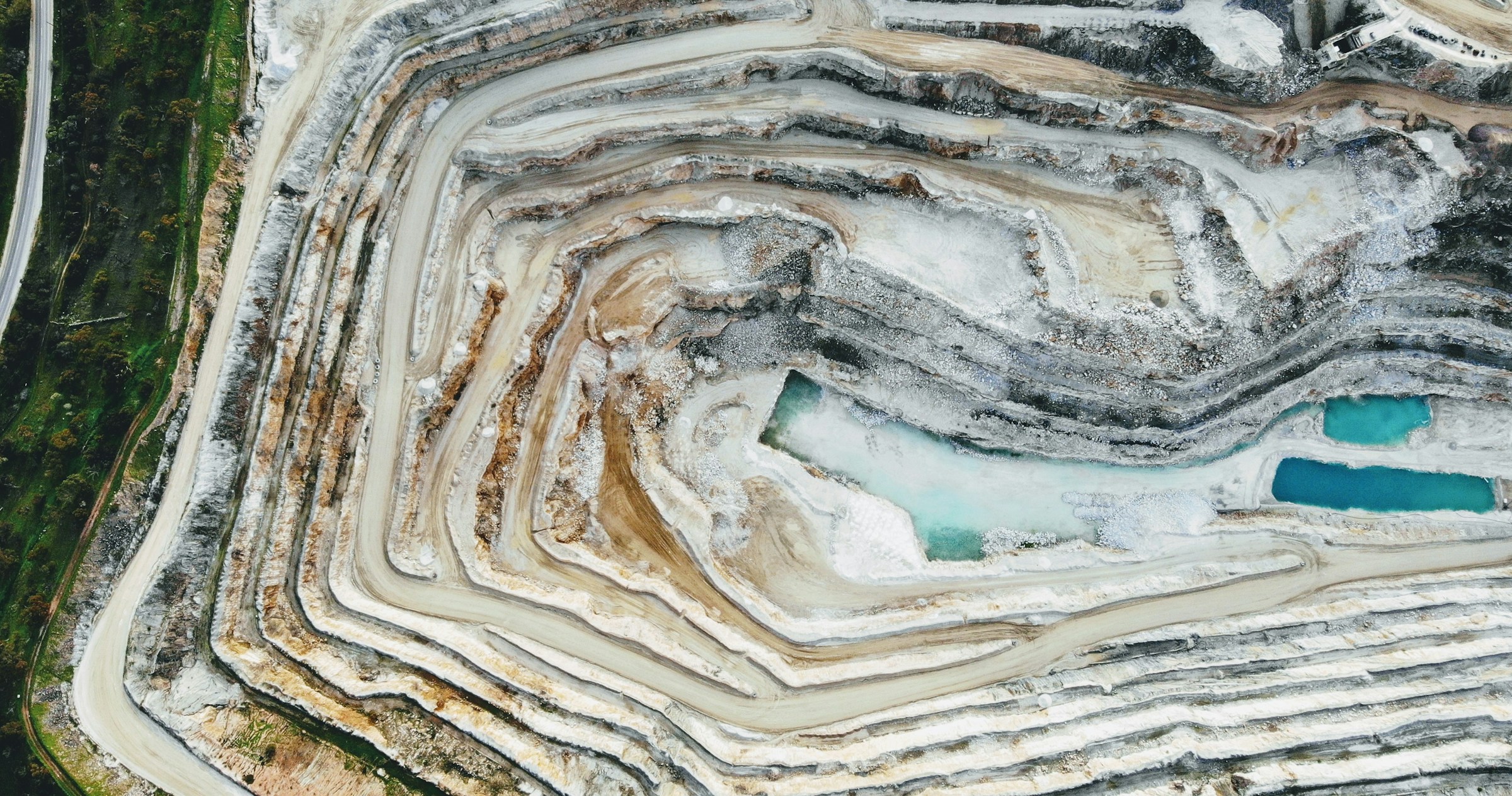 Aerial view of open-pit mine with terraced levels and turquoise water pools
