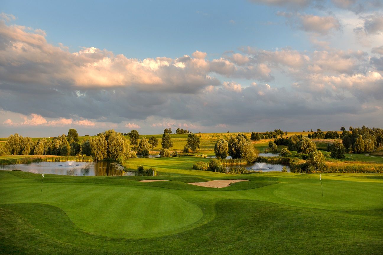 Golfplatz mit Wasserflächen, Bunkern und gepflegten Grüns unter einem dramatischen Wolkenhimmel