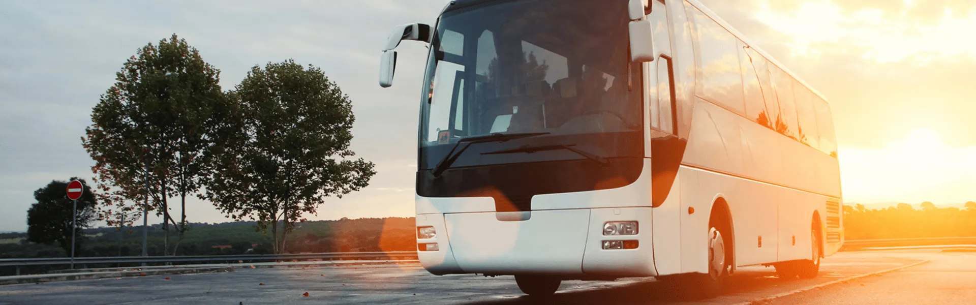 White coach bus driving on a road at sunset