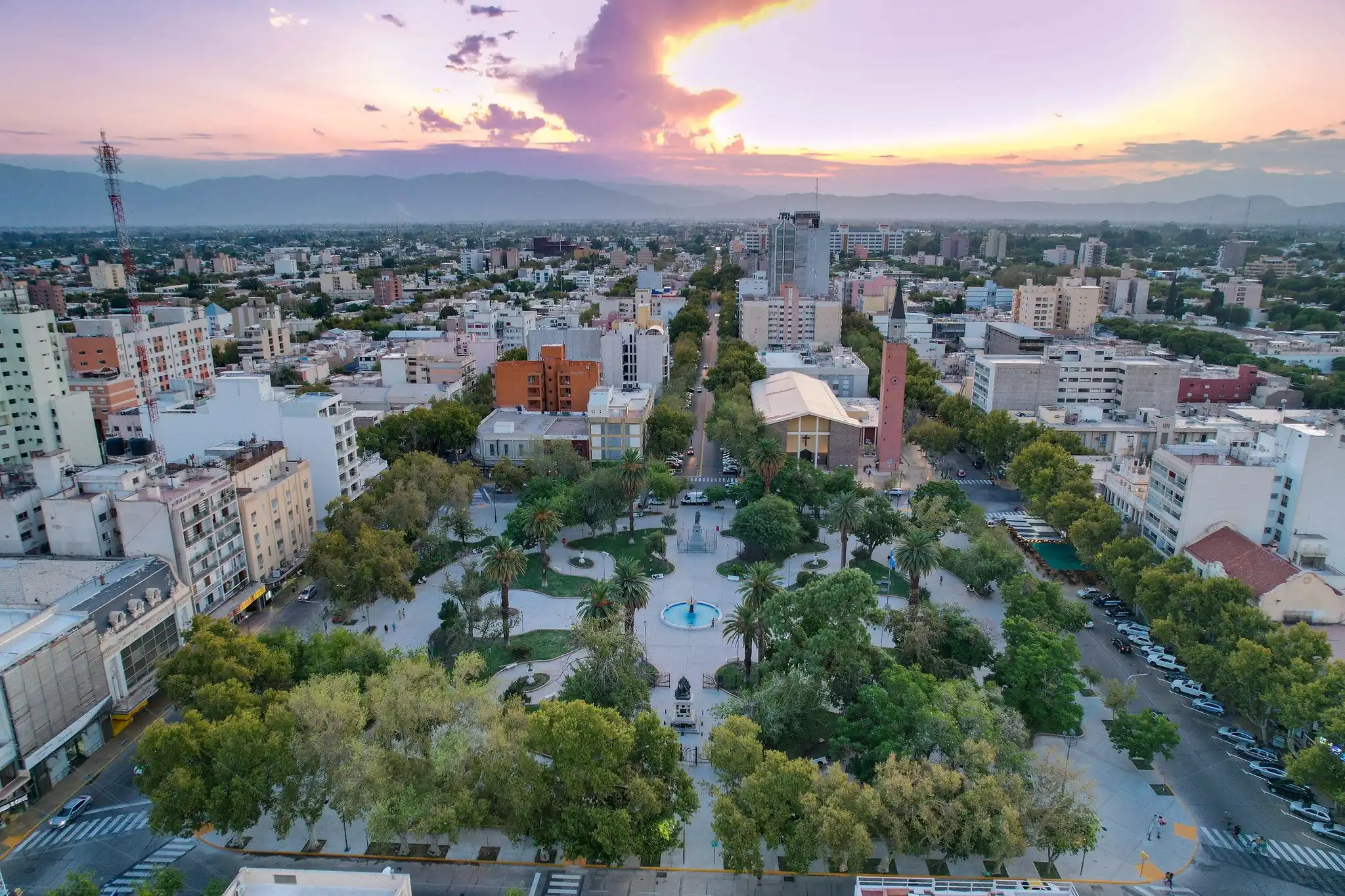 Ciudad al atardecer con vista aérea de plaza central y edificios modernos