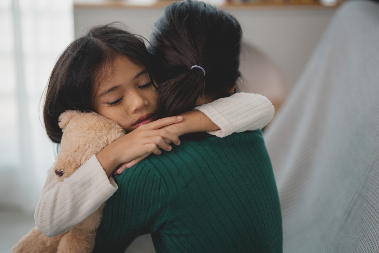 Young child hugging caregiver while holding a teddy bear, representing the human connection in our solutions