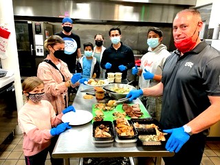 Ian King and volunteers in masks and gloves serving prepared meals in a community kitchen.
