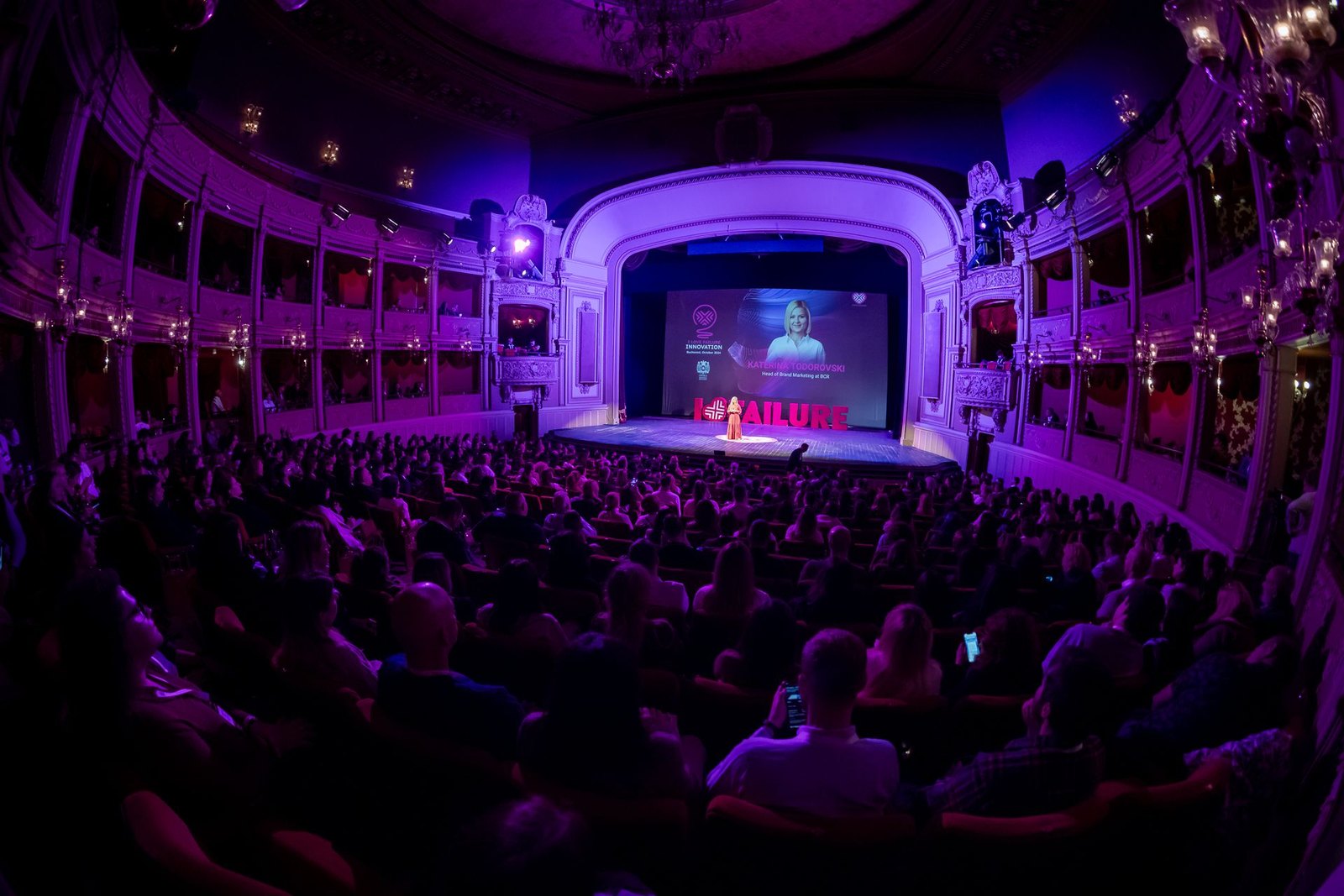 A packed audience watching Katerina speak at I Love Failure in a purple-lit theatre