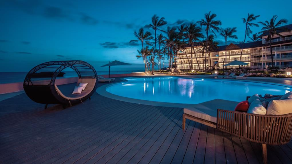 A glowing coastal resort pool beside the ocean at twilight