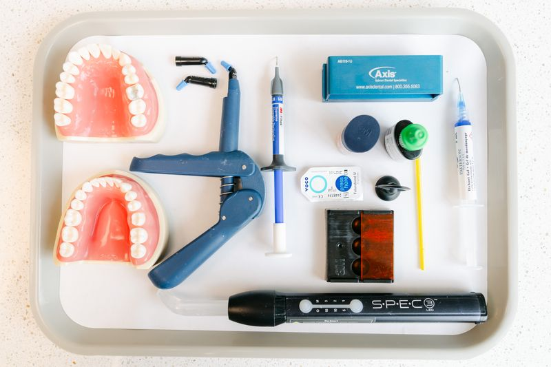 Composite tray setup with two typodonts, composite syringe, dispenser gun, and SPEC 3 curing light