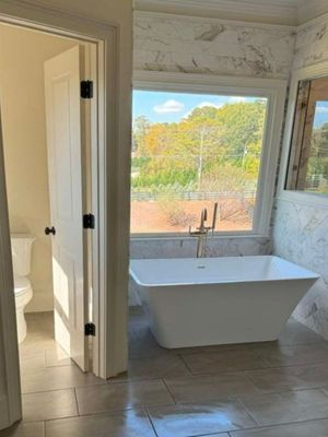 Freestanding white soaking tub under a large window with outdoor view