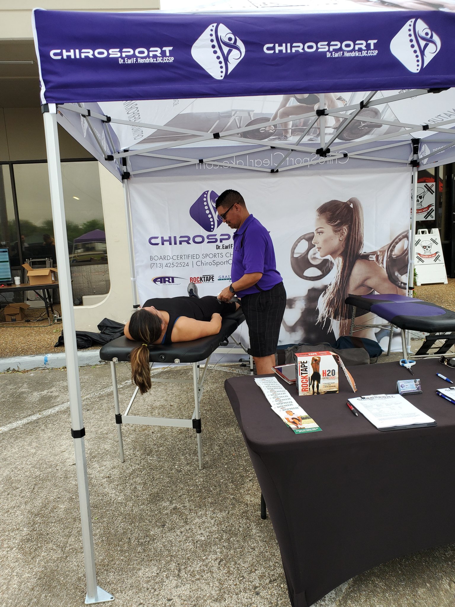 Using a percussion massage tool on a patient lying on the treatment table at an event