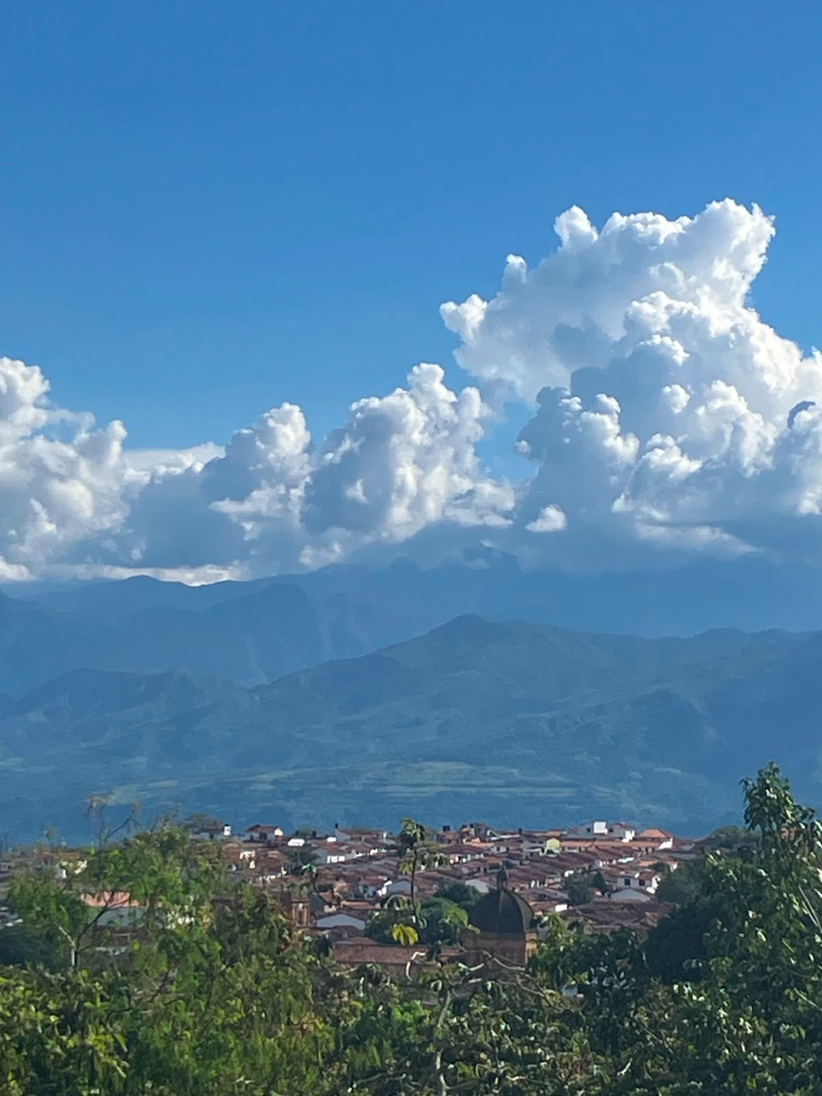Vista panorámica de Barichara con techos de teja, la cúpula de la iglesia, montañas y nubes blancas en cielo azul