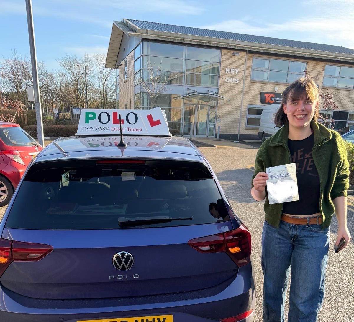 Happy student holding their practical driving test pass certificate by the Polo car